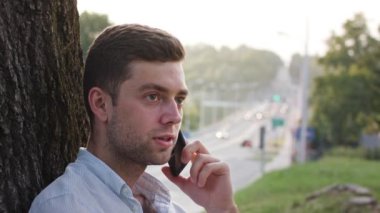 Bir ağacın altında telefonda konuşan bir genç adam