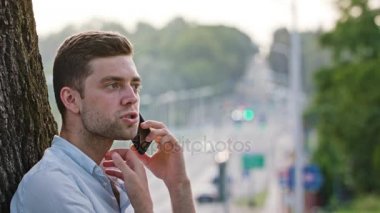 Bir ağacın altında telefonda konuşan bir genç adam