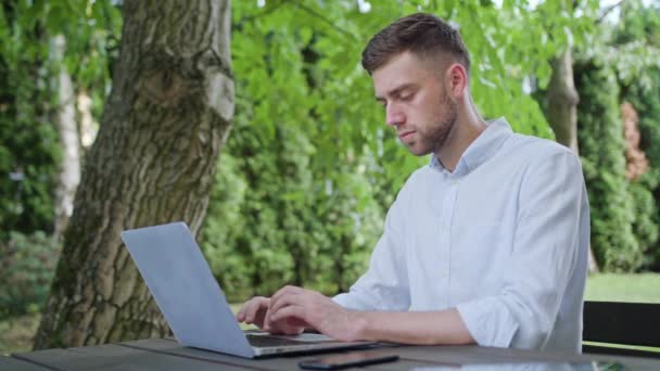 En ung Man använder en bärbar dator i parken — Stockvideo