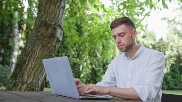 Un giovane che usa un computer portatile nel parco — Video Stock