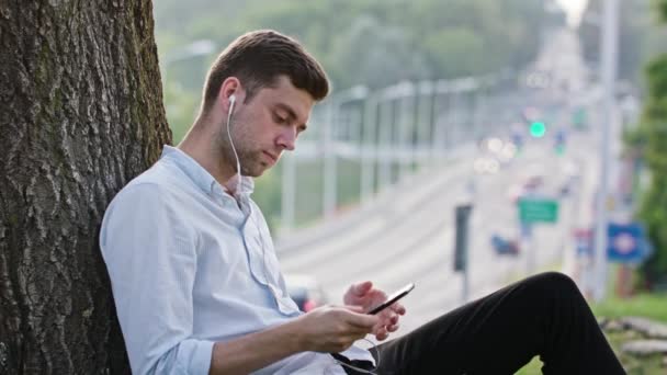 Un joven usando un móvil al aire libre — Vídeos de Stock