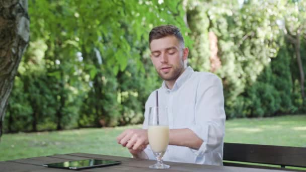 Ein junger Mann trinkt Milchshake im Park — Stockvideo