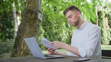 Bir genç adam okuma ve parkta bir dizüstü bilgisayar kullanarak