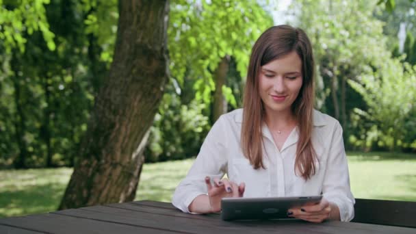 Молода леді використовує iPad в парку — стокове відео