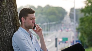 Bir ağacın altında telefonda konuşan bir genç adam
