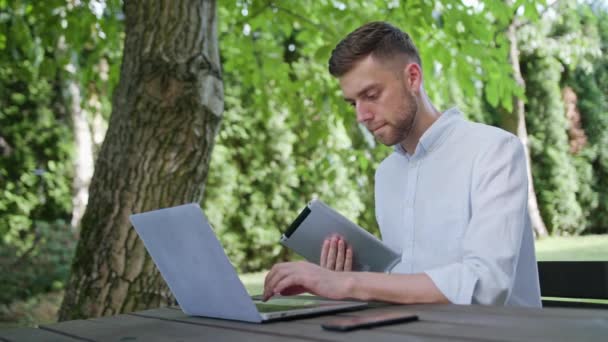 Um jovem usando um laptop e uma tabuleta — Vídeo de Stock