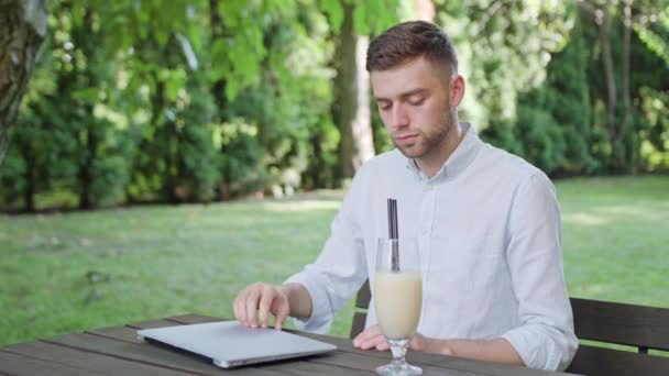 Молодой человек пьет молочный коктейль в парке — стоковое видео