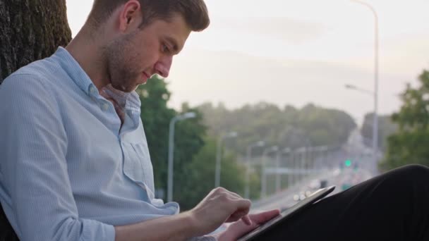 Un joven usando una tableta al aire libre — Vídeos de Stock