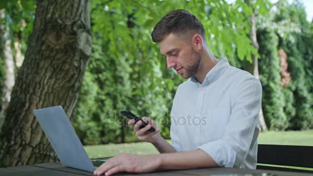 Молодой человек, использующий телефон в парке — стоковое видео