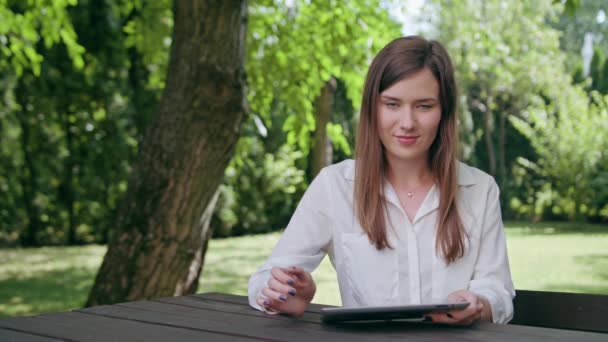 Ung dam med en ipad i parken — Stockvideo