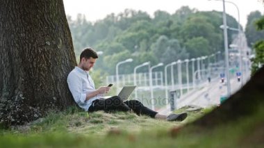 Cep telefonu ve Laptop açık havada kullanan bir genç adam