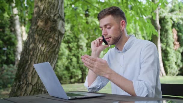 Молодой человек разговаривает по телефону в парке — стоковое видео