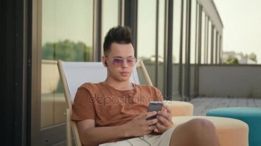 Terasta bir akıllı telefon kullanan bir genç adam.