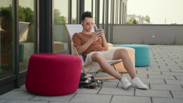 A Young Man Using a Smartphone on the Terrace. — Stock Video