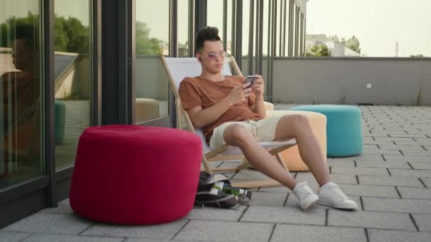 Ein junger Mann mit einem Smartphone auf der Terrasse. — Stockvideo