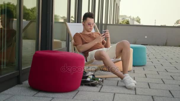Um jovem usando um smartphone no terraço . — Vídeo de Stock