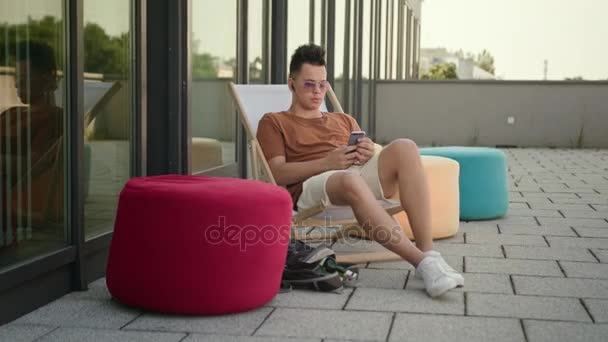 Молодой человек, использующий смартфон на террасе . — стоковое видео