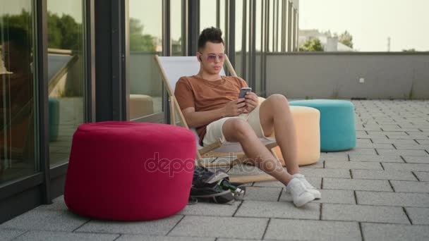 Ein junger Mann mit einem Smartphone auf der Terrasse. — Stockvideo