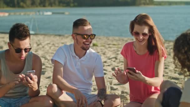 Jóvenes divirtiéndose en la playa usando teléfonos — Vídeo de stock