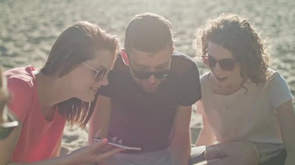 Jovens se divertindo na praia usando telefones — Vídeo de Stock