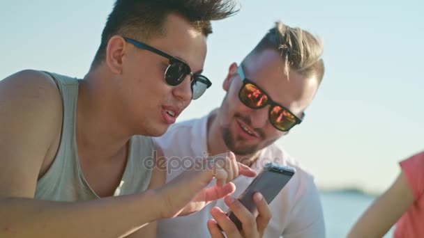 Jóvenes divirtiéndose en la playa usando teléfonos — Vídeos de Stock