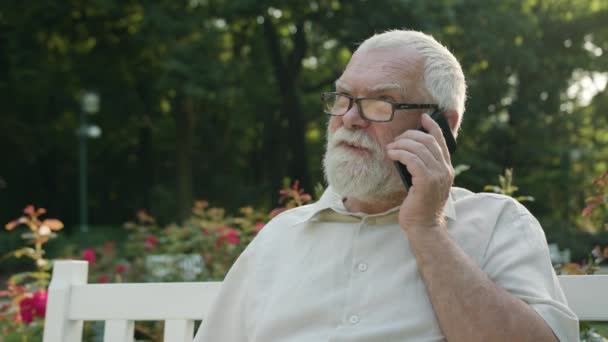 Старик разговаривает по телефону на улице — стоковое видео