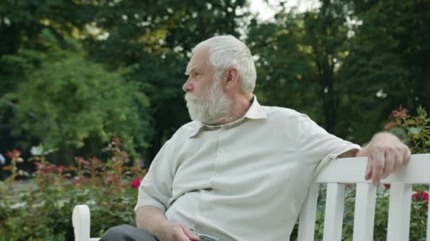 Yaşlı adam parkta beyaz bir bankta oturmuş — Stok video