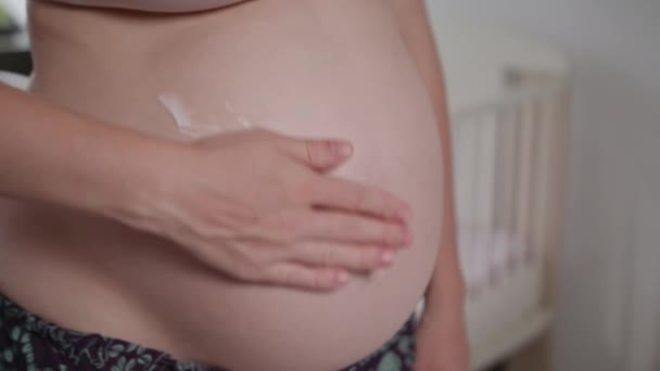 Молодая беременная женщина втирает сливки себе в живот — стоковое видео