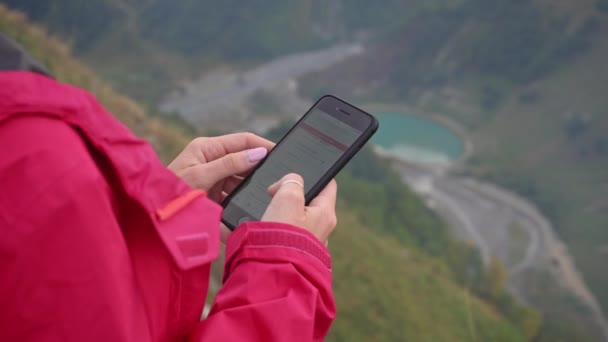 Una joven usando un teléfono móvil en las montañas . — Vídeos de Stock