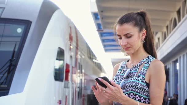 Jonge dame met behulp van een Smartphone op station. — Stockvideo