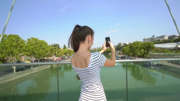 Una giovane signora che scatta foto sul ponte sul fiume — Video Stock