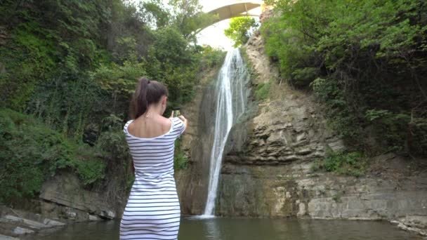 En ung dam att ta foton av ett vattenfall. — Stockvideo