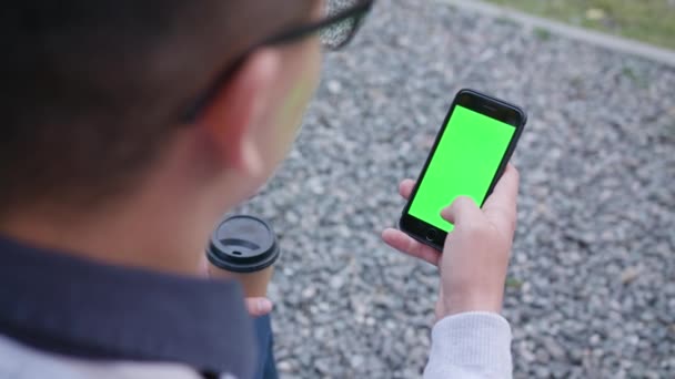Ένας νεαρός άνδρας με ένα τηλέφωνο με μια πράσινη οθόνη — Αρχείο Βίντεο