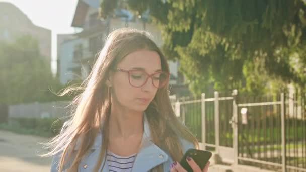 Eine junge Frau, die zu Fuß geht und ein Smartphone benutzt — Stockvideo