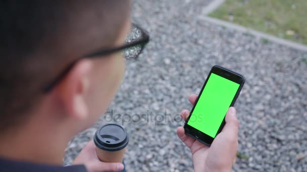 Ένας νεαρός άνδρας με ένα τηλέφωνο με μια πράσινη οθόνη — Αρχείο Βίντεο