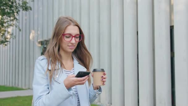 Een jonge dame lopen en met behulp van een Smartphone — Stockvideo