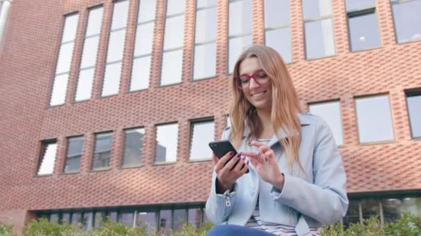 Uma jovem senhora usando um smartphone perto do edifício — Vídeo de Stock