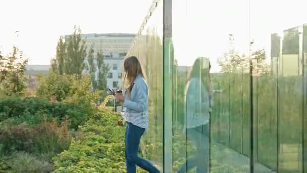 Bir genç bayan yürüyüş ve açık havada bir telefonu kullanarak — Stok video