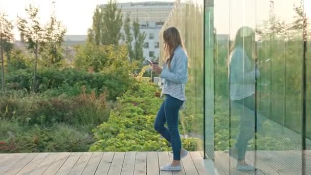 Una joven dama caminando y usando un teléfono al aire libre — Vídeos de Stock