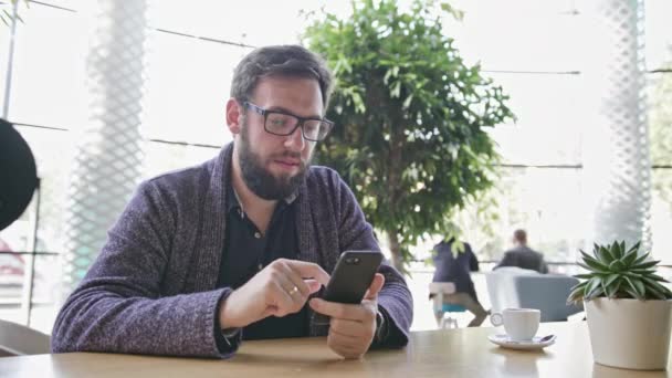 Un joven usando un Smartphone en el Café — Vídeos de Stock