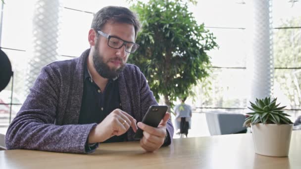 Ein junger Mann mit einem Smartphone im Café — Stockvideo
