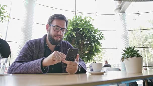 Ein junger Mann mit einem Smartphone im Café — Stockvideo