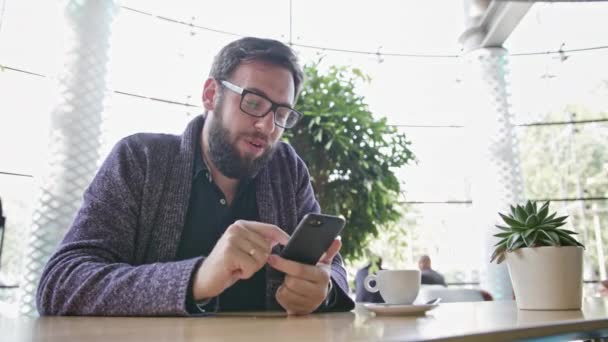Ein junger Mann mit einem Smartphone im Café — Stockvideo