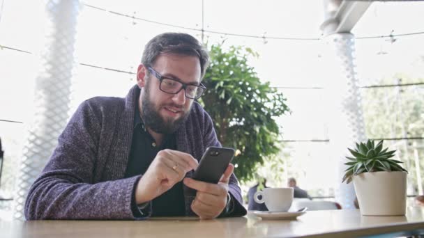 Un joven usando un Smartphone en el Café — Vídeos de Stock