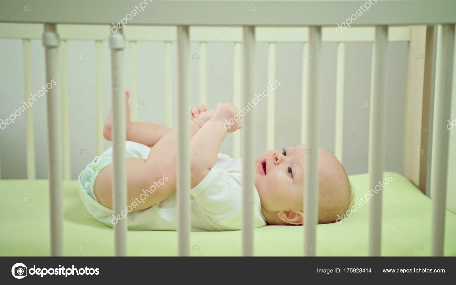Baby Lying In A Crib At Home Eating Its Toes Stock Photo