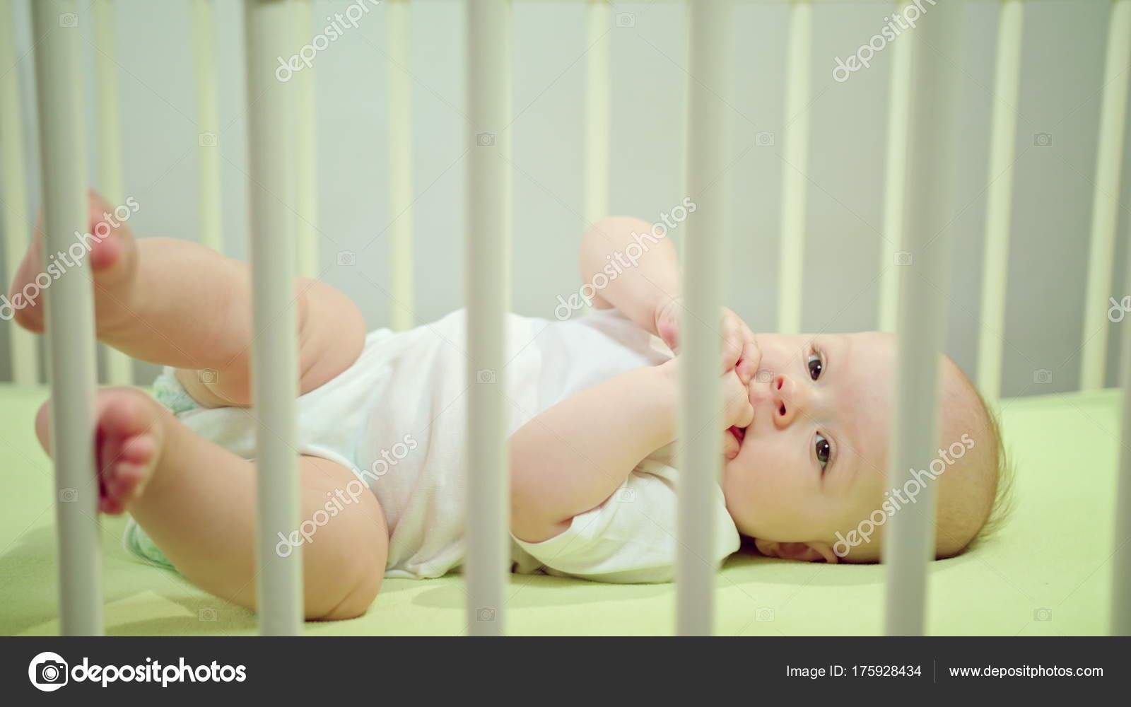 Baby Lying In A Crib At Home Eating Its Fingers Stock Photo
