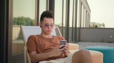 Terasta bir akıllı telefon kullanan bir genç adam.