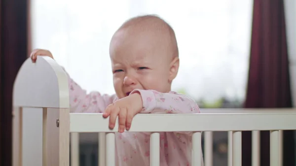 Bebê em pé em um berço em casa. Chorando — Fotografia de Stock