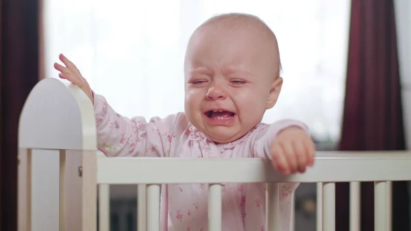 Bebê em pé em um berço em casa. Chorando — Fotografia de Stock