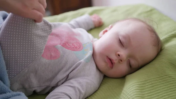 Kvinnliga händer som täcker en bebis i sängen — Stockfoto
